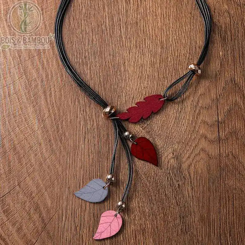 collier pendentif feuilles en bois coloris rouge bordeaux gris rose sur cordon multibrin noir fond bois