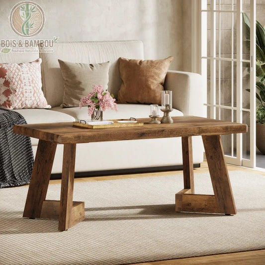 Table en bois massif basse style farmhouse 1. Table basse de salon en bois massif au style farmhouse avec un plateau épais et des pieds originaux en biais, décorée de fleurs et bougies devant un canapé.