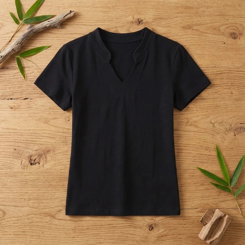 T-shirt femme col V noir en coton et fibre de bambou posé à plat sur une table en bois brut avec feuilles de bambou
