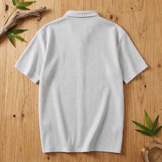 Polo homme en maille de bambou vu de dos, posé à plat sur une table en bois brut avec feuilles de bambou