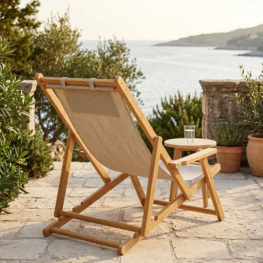 Transat en toile et bambou à accoudoirs vu de dos, cadre naturel et toile beige, sur une terrasse en pierre face à la mer