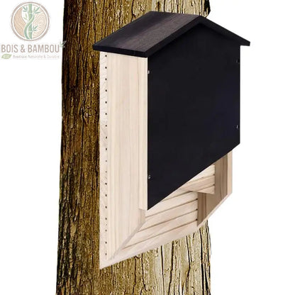Abri pour chauve-souris en bois à toit noir fixé sur un tronc d'arbre au jardin