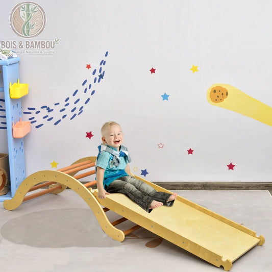 Aire de Jeux 3-en-1 en Bois. Un jeune enfant s'amuse sur une structure de motricité en bois clair comprenant une rampe de glisse et un pont à barreaux, dans une chambre décorée.
