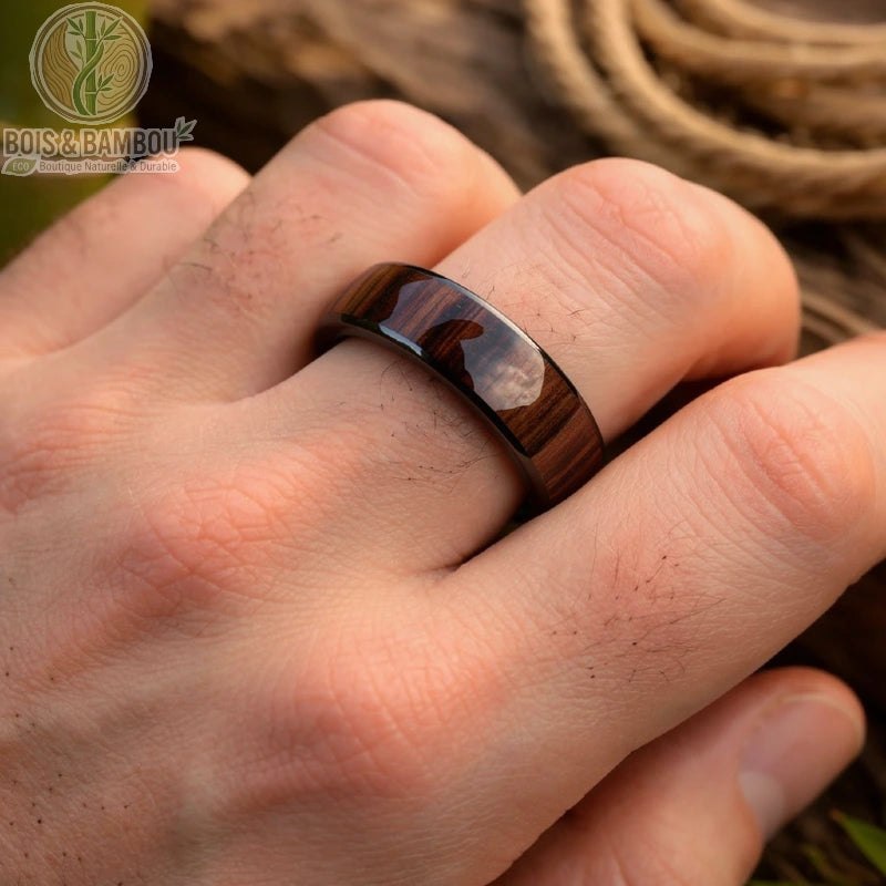 Alliance en tungstène et bois foncé portée sur une main d’homme, anneau brillant avec finition lisse sur fond naturel bois et corde

