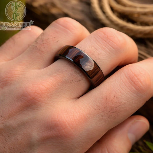 Alliance en tungstène et bois foncé portée sur une main d’homme, anneau brillant avec finition lisse sur fond naturel bois et corde
