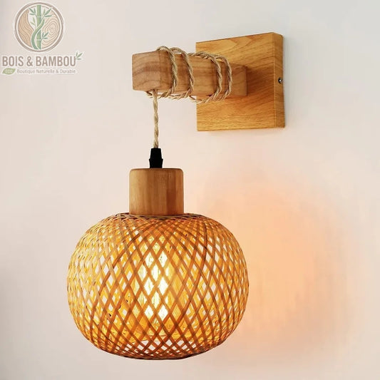 Applique murale lanterne en bambou tressé, suspendue à une potence en bois naturel par un cordon tressé assorti.