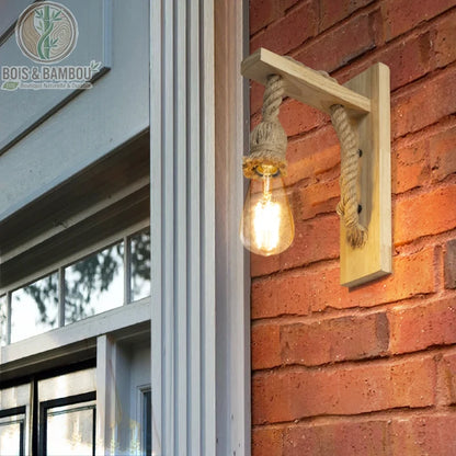 Applique Murale en Bois Rétro, un luminaire d'extérieur rustique composé d'un support en bois clair et d'une grosse corde de chanvre soutenant une ampoule vintage, installé sur un mur en briques rouges.