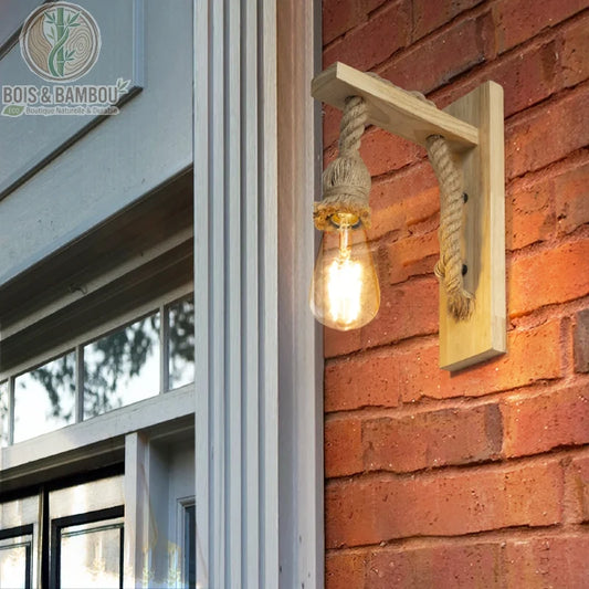 Applique Murale en Bois Rétro, un luminaire d'extérieur rustique composé d'un support en bois clair et d'une grosse corde de chanvre soutenant une ampoule vintage, installé sur un mur en briques rouges.