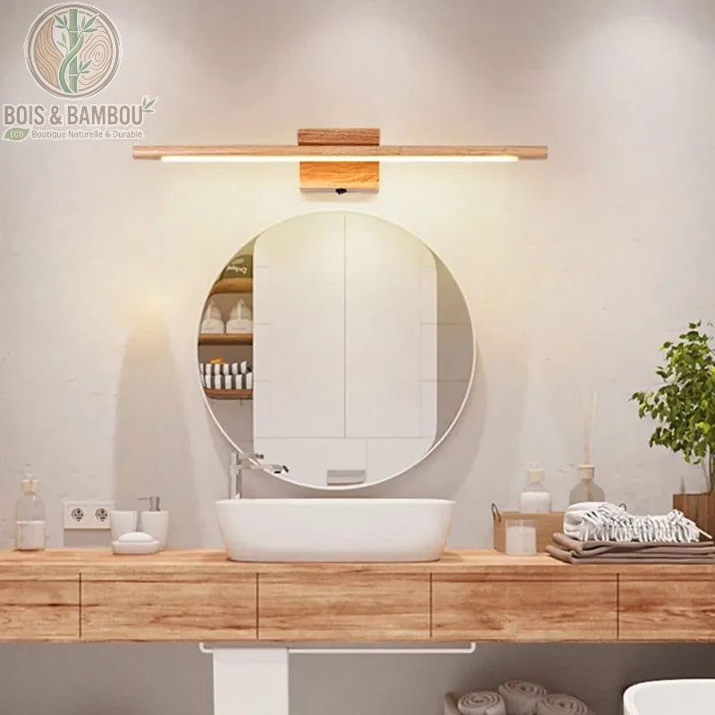 Applique murale en bois massif , un luminaire de salle de bain linéaire et minimaliste en bois clair, installé au-dessus d'un miroir rond pour un éclairage doux et naturel.