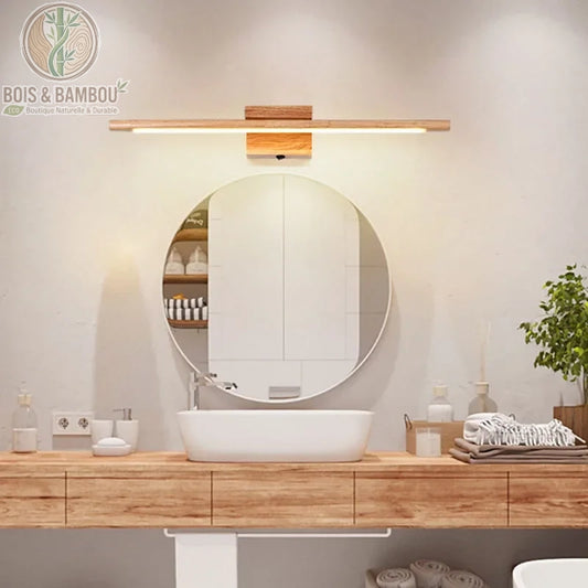 Applique murale en bois massif , un luminaire de salle de bain linéaire et minimaliste en bois clair, installé au-dessus d'un miroir rond pour un éclairage doux et naturel.
