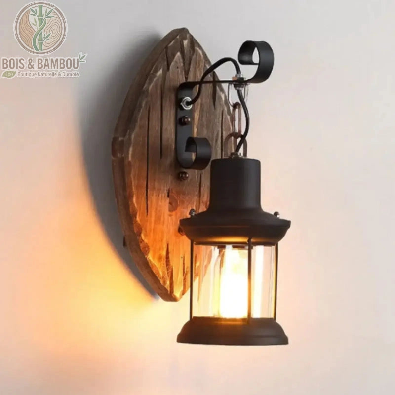 Applique murale industrielle en bois , une lanterne vintage en métal noir suspendue à un support mural en bois brut sculpté, diffusant une lumière chaude et tamisée.