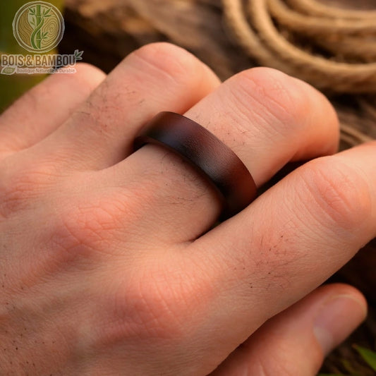 Bague en bois de santal naturel portée sur une main d’homme, anneau en bois sombre au design lisse avec fond naturel bois et bambou.

