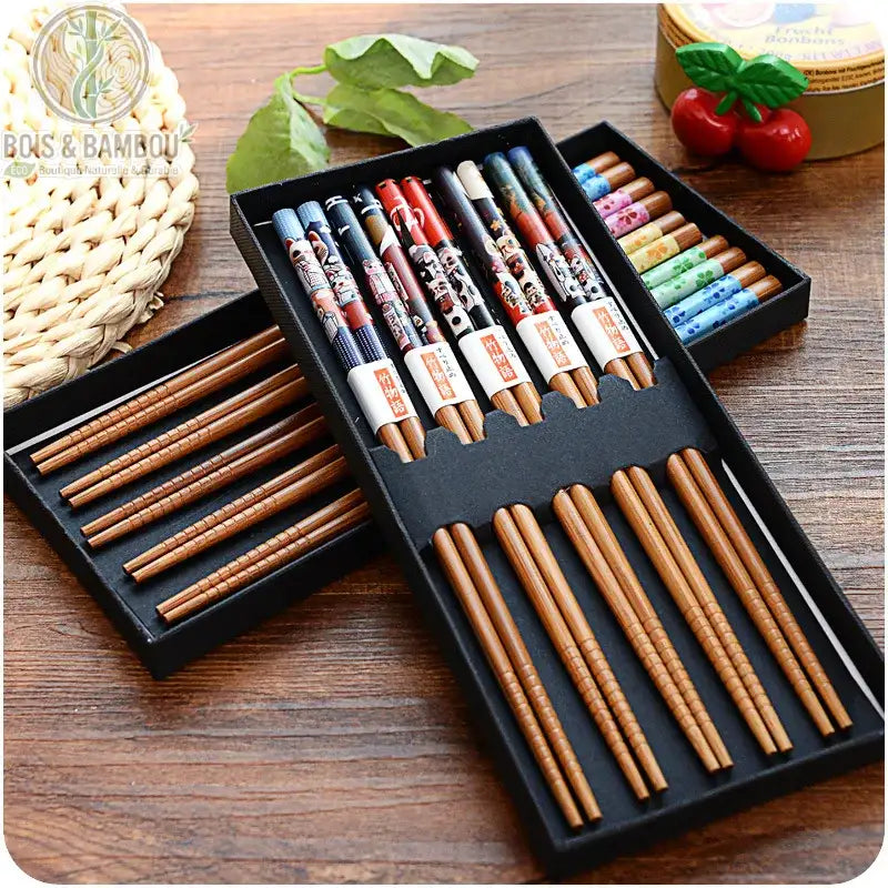 Baguettes en bambou naturel antidérapantes. Plusieurs paires de baguettes aux motifs colorés et variés, présentées dans des coffrets noirs sur une table en bois. Style traditionnel.