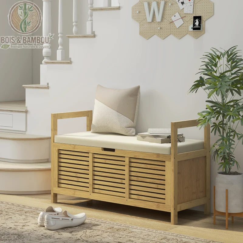 Banc à chaussures en bambou avec coffre de rangement. Un banc élégant en bois clair avec assise rembourrée et façades à lattes, placé au pied d'un escalier dans une entrée lumineuse.
