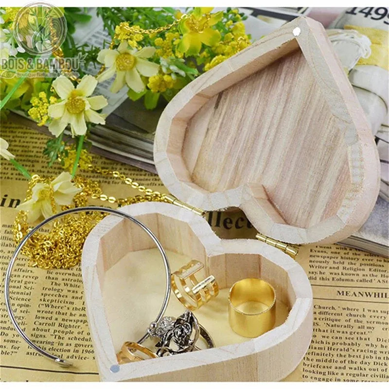 Boîte cœur en bois naturel ouverte avec bagues et collier doré sur fond de fleurs jaunes
