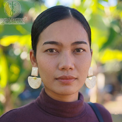 Boucles d'oreilles bohèmes en bois et raphia blanc de forme demi-lune portées par une femme en gros plan, avec un arrière-plan naturel flou.