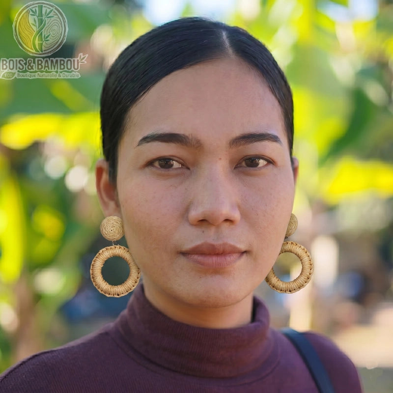 Boucles d'oreilles bohèmes en rotin et bois circulaires portées par une femme en gros plan, avec un arrière-plan naturel flou.