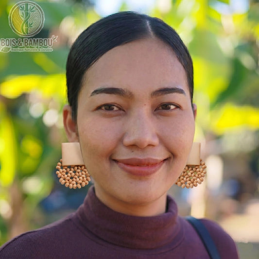 Boucles d'oreilles en perles de bois marron portées par une femme souriante, avec des perles en grappe et un arrière-plan naturel flou.