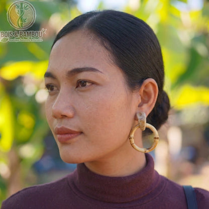 Boucles d'oreilles pendantes en bambou circulaires portées par une femme, mettant en avant un style naturel et artisanal sur un fond ensoleillé.