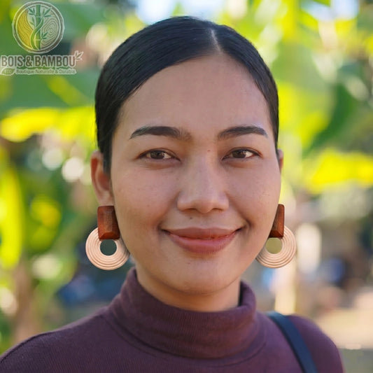 Boucles d'oreilles rondes en bois ethniques portées par une femme souriante en gros plan, avec des anneaux clairs striés et un arrière-plan flou.