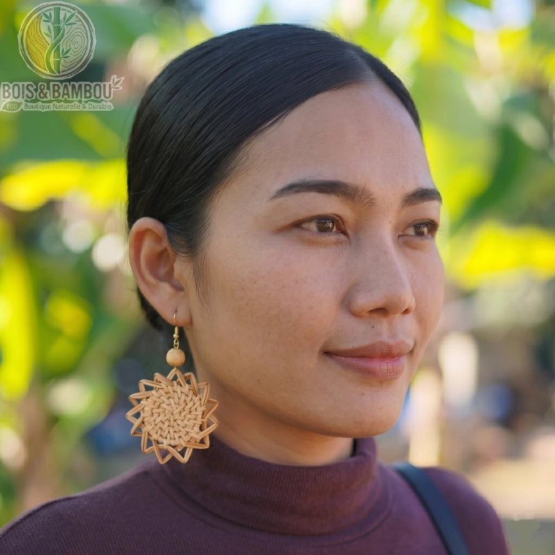 Boucles d'oreilles tissé en bois et rotin de forme étoilée portées par une femme de profil, avec un arrière-plan naturel flou.