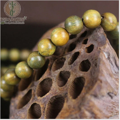 Gros plan perles mala santal vert Verawood 8 mm nuances vert olive et doré sur bois sculpté fond brun