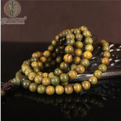 Mala santal vert naturel 108 perles Verawood couleur verte posé sur support bois sculpté fond brun