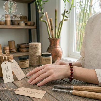Bracelet bouddhiste en bois de santal rouge porté au poignet, posé sur un établi avec des outils de sculpture et des étiquettes.