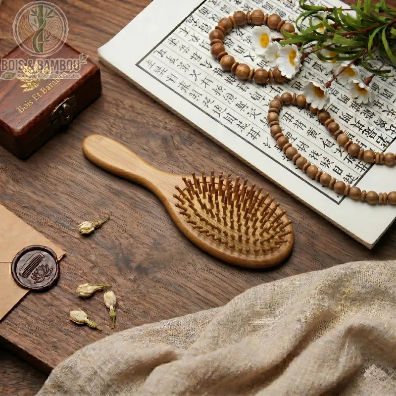 Brosse à cheveux professionnelle en bambou. Brosse ovale en bois sur table avec calligraphie chinoise, fleurs et perles. Accessoire durable pour massage du cuir chevelu et démêlage.