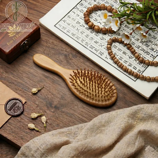 Brosse à cheveux professionnelle en bambou. Brosse ovale en bois sur table avec calligraphie chinoise, fleurs et perles. Accessoire durable pour massage du cuir chevelu et démêlage.