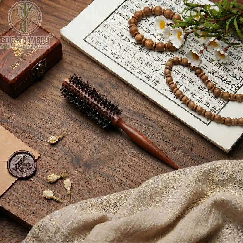 Brosse à cheveux ronde en poils de sanglier et manche en bois posée sur une table avec décor zen, calligraphie et perles. Accessoire professionnel pour brushing et volume naturel.
