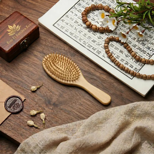 Brosse en Bambou Naturel sur une table en bois avec calligraphie, perles et fleurs. Accessoire de coiffure écologique pour un brossage doux et naturel du cuir chevelu.