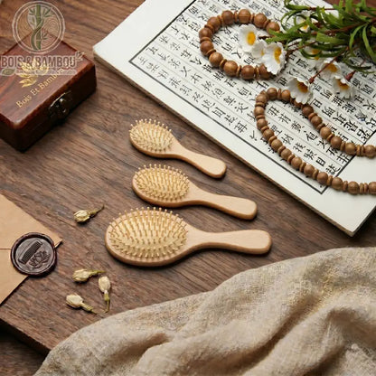 Brosse en Bois de Hêtre. Trois brosses en bois de hêtre de tailles différentes posées sur une table en bois avec décor calligraphie et perles. Accessoire de beauté naturel.
