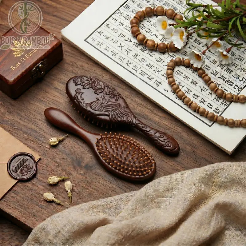 Brosse en Bois de Santal Sculptée avec motif de phénix. Posée sur table bois avec rouleau calligraphie, perles, fleurs blanches, tissus, cachet de cire. Accessoire beauté luxe bio.