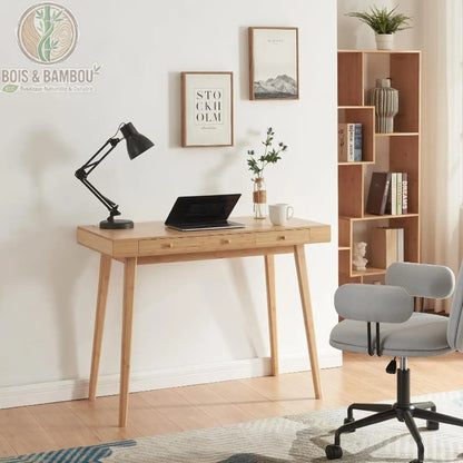 Bureau Scandinave en Bambou. Un bureau épuré en bois clair avec tiroirs, équipé d'une lampe noire et d'un ordinateur, accompagné d'une chaise grise et d'une étagère assortie.