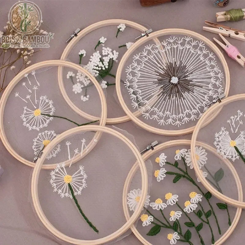 Cadre de broderie en bambou naturel mettant en valeur des motifs floraux délicats, tels que des pissenlits et des marguerites, brodés sur un voile de tulle transparent.