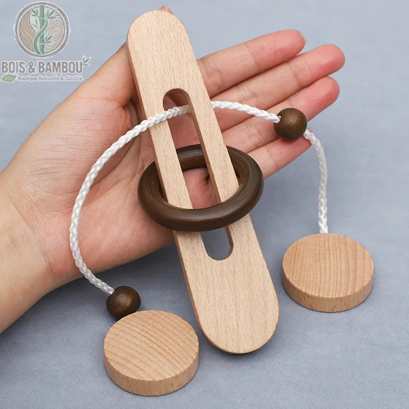 Casse-tête anneau magique en bois. Un puzzle traditionnel composé d'une pièce plate percée, d'un anneau sombre et d'une cordelette blanche avec perles, tenu dans une main.