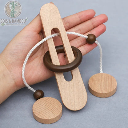 Casse-tête anneau magique en bois. Un puzzle traditionnel composé d'une pièce plate percée, d'un anneau sombre et d'une cordelette blanche avec perles, tenu dans une main.