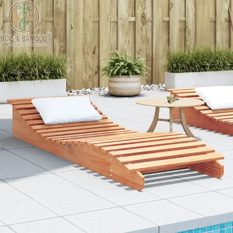 Chaise Longue en Pin Massif. Un bain de soleil robuste en lattes de pin clair avec coussin blanc, installé sur une terrasse en dalles grises près d'une piscine et d'une clôture.