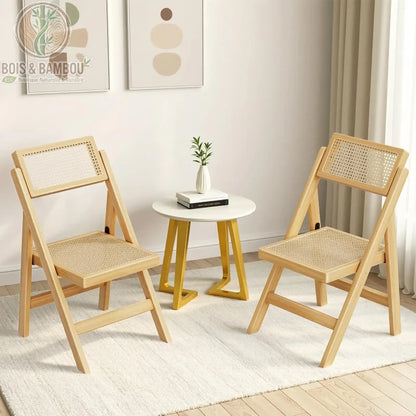 Chaise Pliante en Rotin. Deux chaises pliantes en bois clair avec dossier et assise en rotin tressé, disposées autour d'une petite table ronde dans un intérieur moderne et épuré.