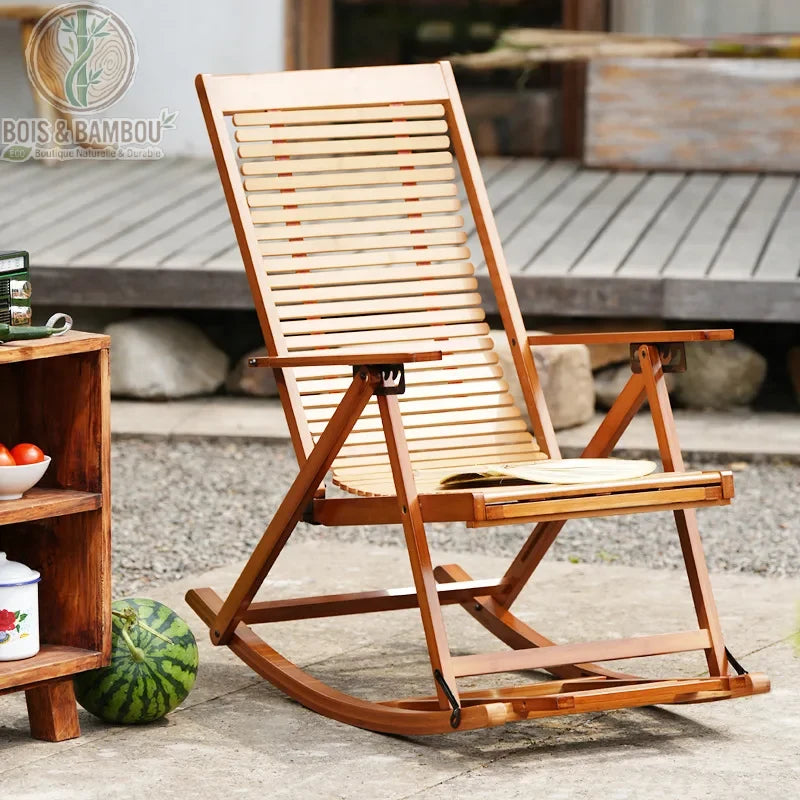 Chaise de Détente en Bambou. Un fauteuil à bascule pliant en lattes de bambou clair, doté d'accoudoirs, installé sur une terrasse à côté d'un meuble en bois et d'une pastèque.