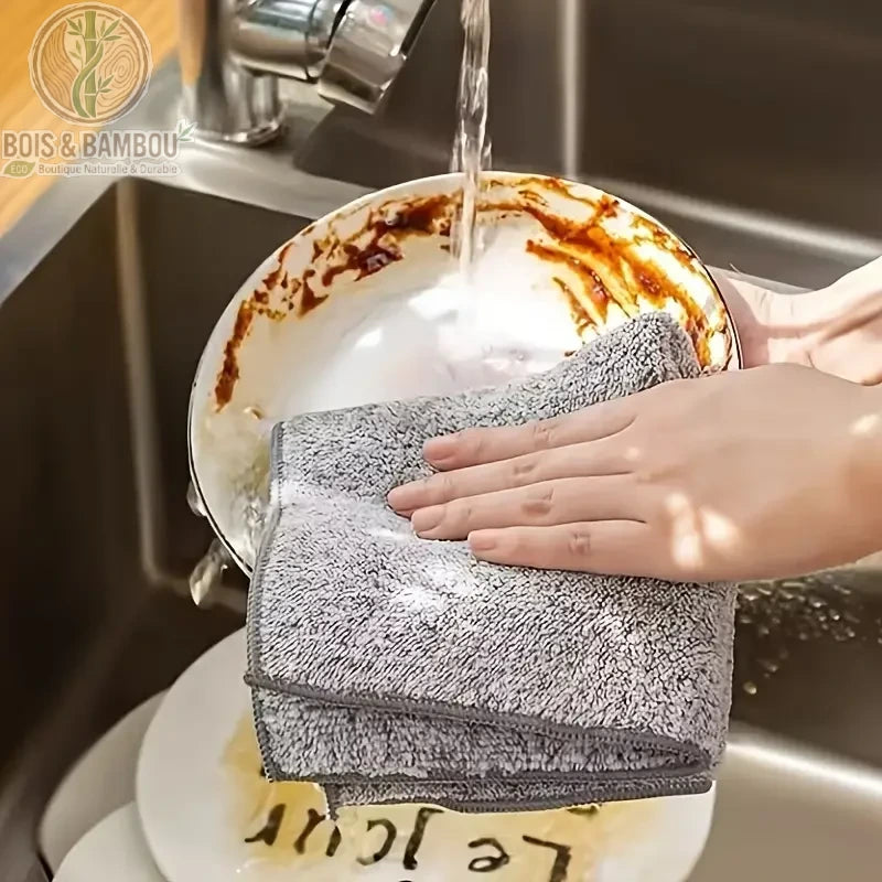 Chiffon en Charbon de Bambou. Une main essuie une assiette très sale avec un chiffon en microfibre gris foncé texturé dans un évier. Alternative écologique et durable pour la vaisselle.