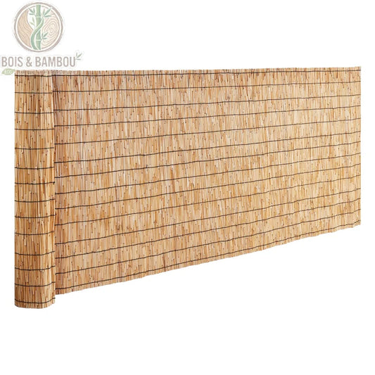 Clôture en Roseau Naturel. Un rouleau de canisse en roseaux naturels liés par des fils horizontaux, partiellement déroulé pour former un écran de protection, présenté sur fond blanc.