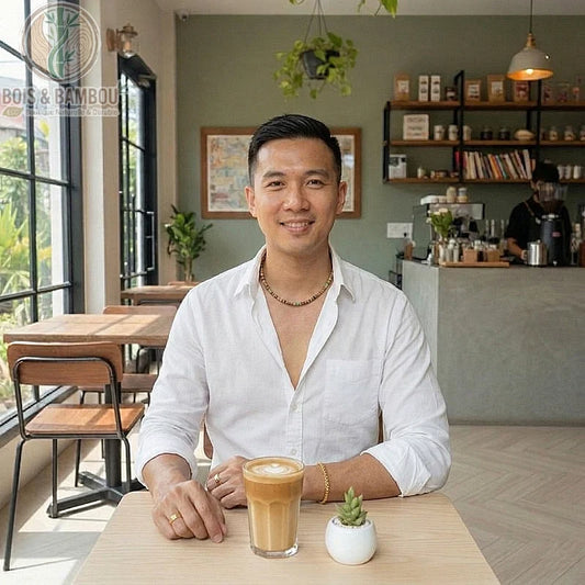 Collier court en perles de coco et bois porté par un homme assis dans un café, devant un latte art et une petite plante.
