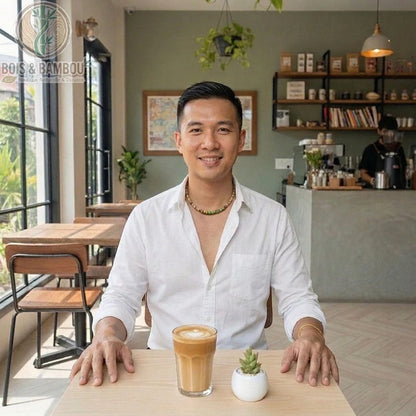 Collier en bois naturel pour homme avec perles colorées, porté par un client souriant dans un café devant un latte.
