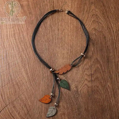 collier pendentif feuilles en bois coloris brun orange et gris vert trois feuilles sur cordon noir fond bois