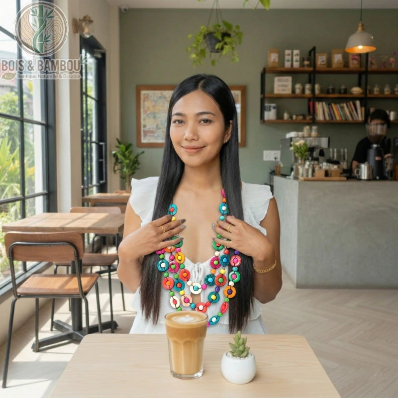 Collier multicouche en perles de bois colorées porté par une femme dans un café, assis devant un latte et une plante.