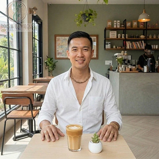 Collier ras du cou en bois de wengé porté par un homme dans un café, assis devant un café latte et une petite plante grasse.