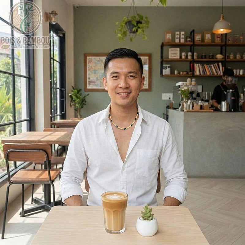 Collier ras du cou en perles de bois blanc porté par un homme en chemise blanche dans un café, devant un latte art.