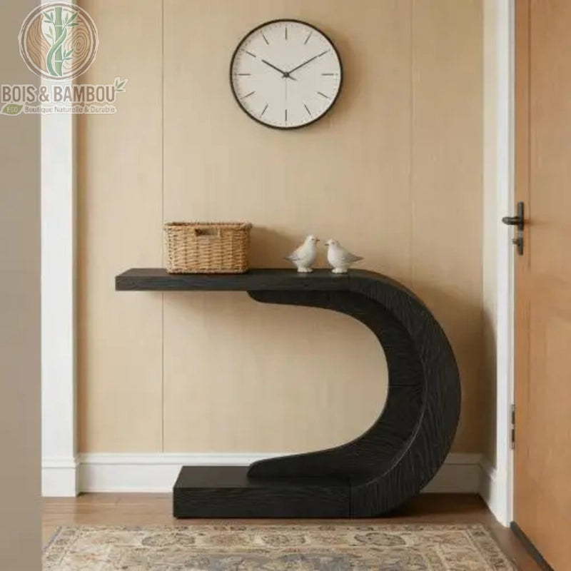 Console En Bois Massif Moderne En Forme De C noir. Console d'entrée design sculpturale en bois noir aux lignes courbes fluides, décorée d'un panier et de figurines sous une horloge murale épurée.
